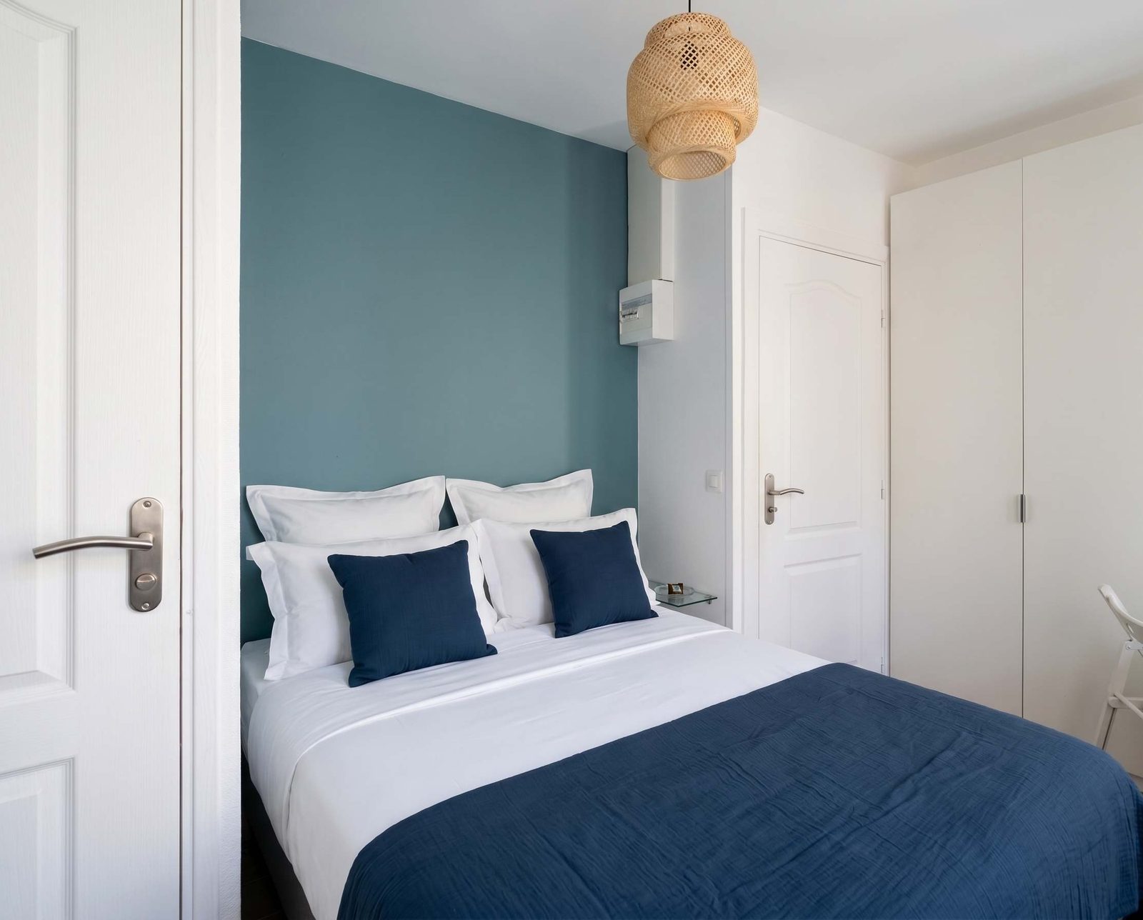 Chambre bleu marine, literie blanche et suspension en rotin