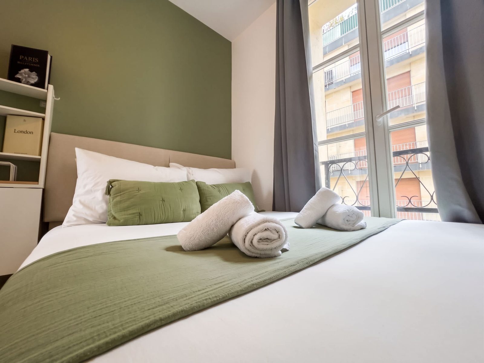 Lit aux coussins vert sauge devant de grandes fenêtres