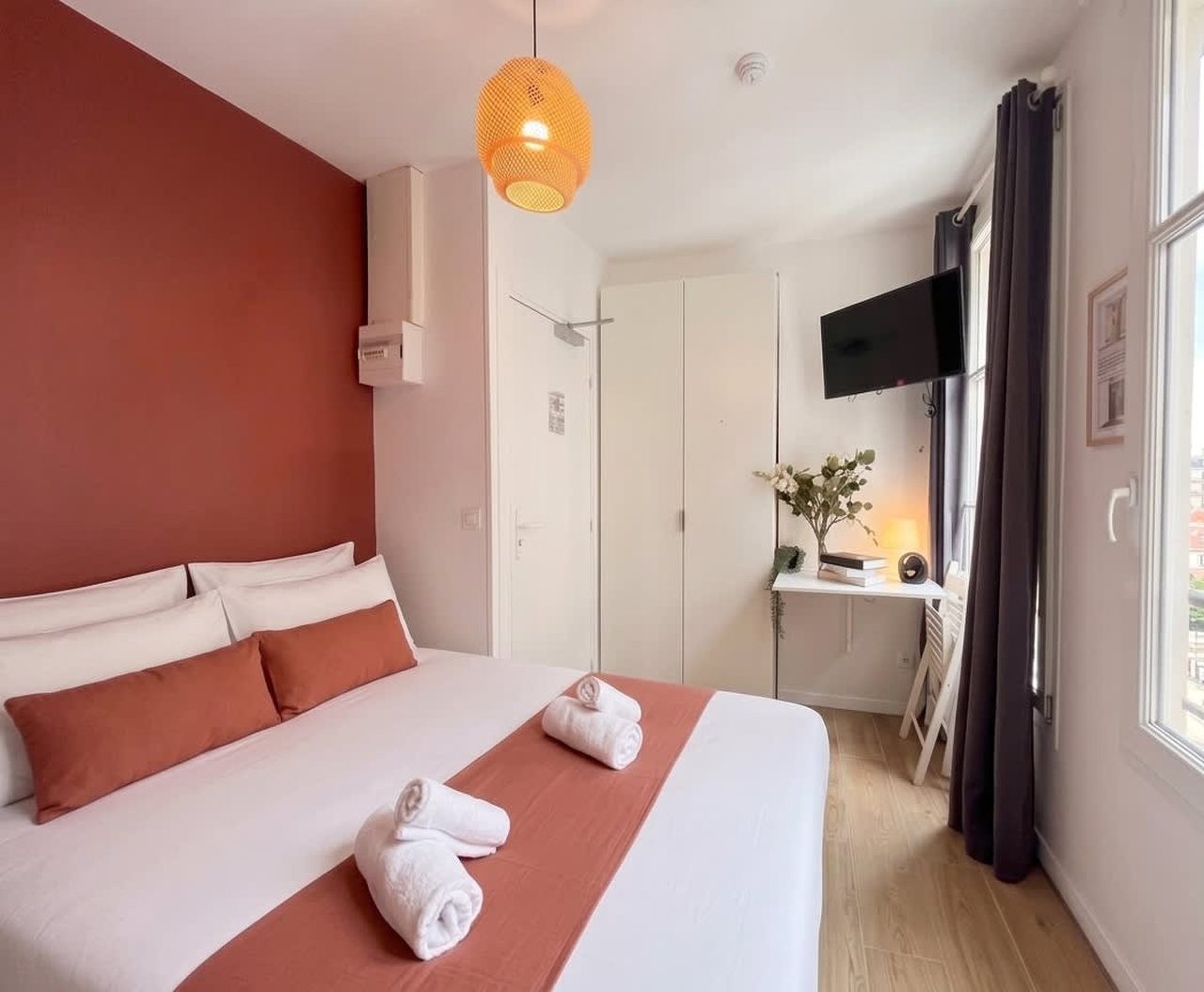Chambre aux tons terracotta, lit dressé de blanc et suspension en rotin