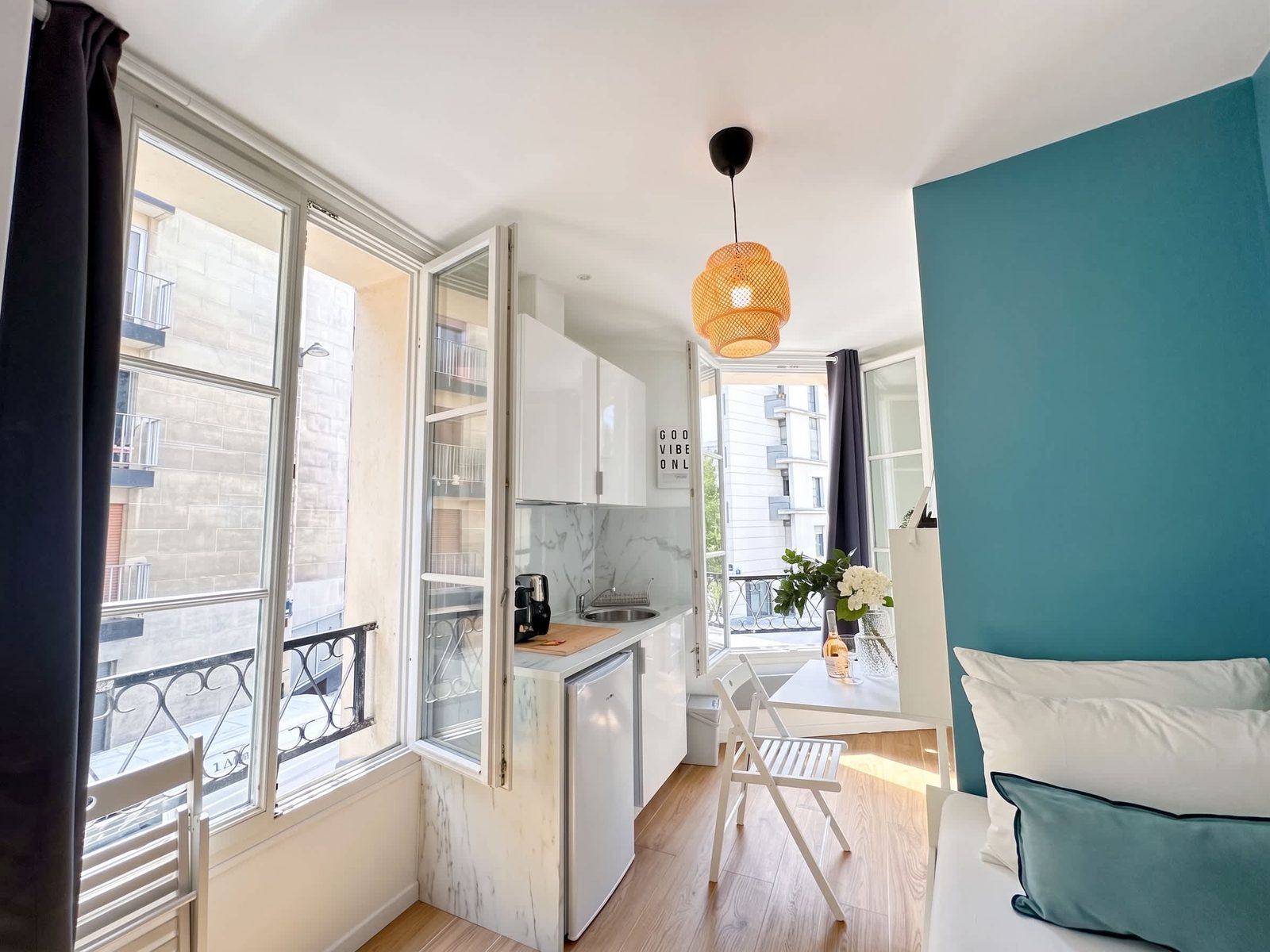 Chambre lumineuse aux hautes fenêtres parisiennes et mur turquoise